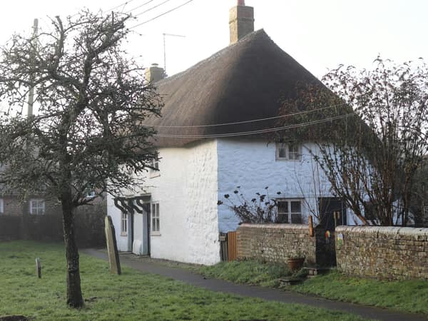 A white thatched cottage behind a stone wall